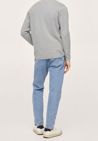 Pull gris à manches longues, tissu léger, coupe décontractée ; associé à un jean en denim bleu clair, jambes légèrement fuselées, et chaussures blanches.