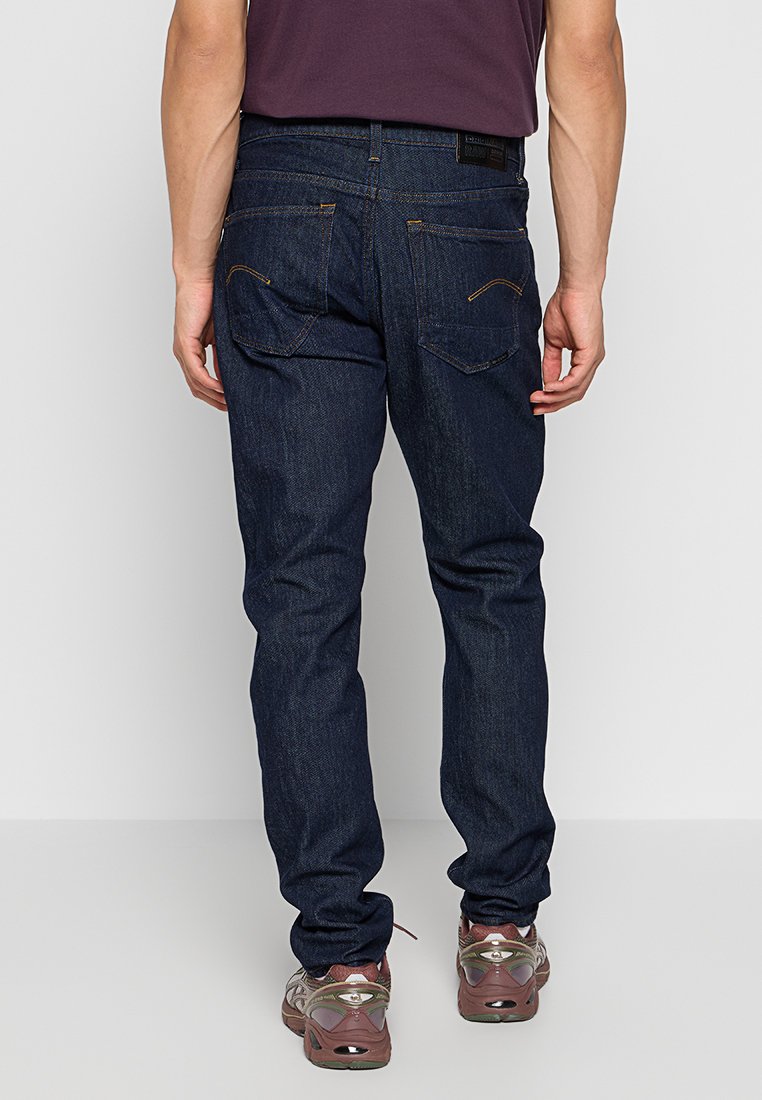 Jeans in denim blu scuro con taglio dritto, dotati di tasche posteriori con dettagli di cucitura discreti e un'etichetta in pelle sulla vita.