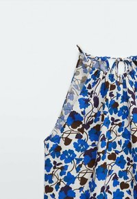 Top senza maniche realizzato in tessuto leggero, con un motivo floreale blu e marrone su uno sfondo chiaro, con scollatura legata.