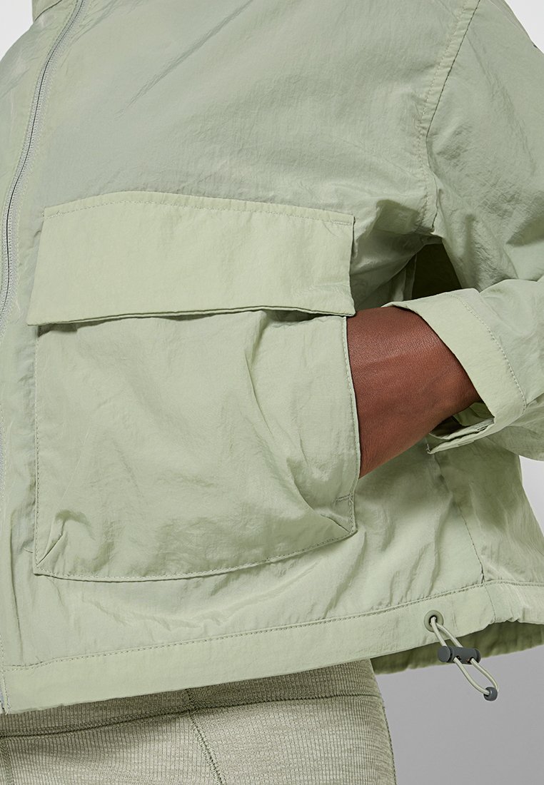 Veste verte claire avec fermeture éclair, poche avant surdimensionnée et cordon élastique à l'ourlet, fabriquée dans un matériau texturé et léger.