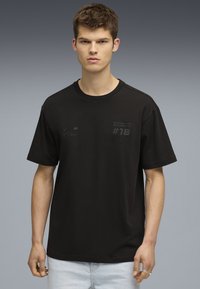 Svart bomull t-shirt med korta ärmar. Har ett strukturerat tryck med "#18" och BMW-logotypen på bröstet. Standard passform och rundad halsringning.