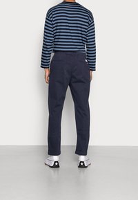 Marinblå tapered byxor i bomull med en slät yta och två bakfickor. Kombineras med en randig långärmad topp.