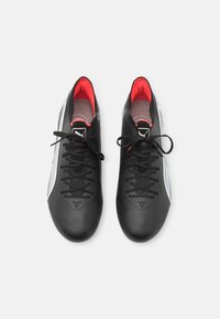 Zapatos sintéticos negros con acentos rojos, que presentan un diseño elegante, superficie texturizada y un sistema de cordones tradicional. Panel lateral blanco.
