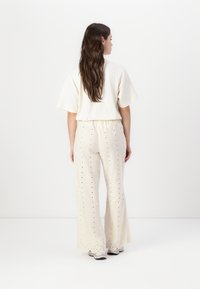 Haut crème à manches courtes associé à un pantalon crème ample et brodé avec des détails en œillets et des ourlets ondulés. Chaussures décontractées visibles.