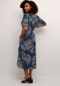 Abito midi blu navy con stampa paisley bianca, maniche corte, scollatura rotonda e vestibilità allentata. Indossato con sandali neri con tacco a strappo.
