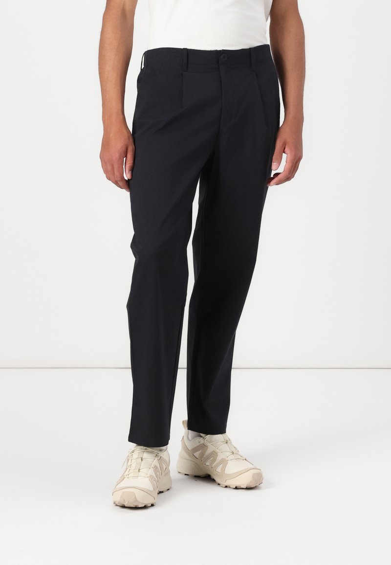 Black tailored pants with a straight leg design, featuring front pleats, side pockets, and a smooth fabric texture. Worn with neutral sneakers.