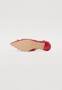 Scarpa con tacco alto in vernice rossa, con punta affusolata, piccolo dettaglio a fiocco e suola color nude. Finitura lucida e design elegante.