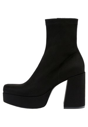 Czarny zamszowy botek za kostkę z masywnym wysokim obcasem i platformą, design typu slip-on oraz gładkim, zaokrąglonym noskiem.