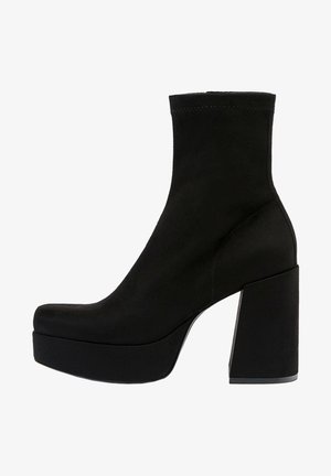 Bottine en daim noir avec talon haut épais et semelle plateforme, design facile à enfiler, bout lisse et arrondi.