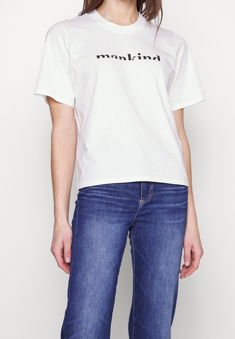Witte katoenen t-shirt met korte mouwen en een ronde hals, met de tekst "mankind" in het zwart over de voorkant gedrukt. Draag het met blauwe spijkerbroeken.