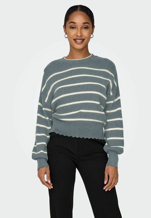 Stripet pullover-sweater med ribbet tekstur i teal med creme striber, brede ærmer og bølget kant, parret med sorte bukser.