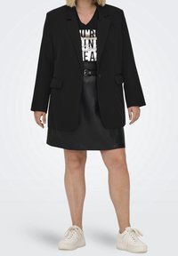 Svart blazer med skräddarsydd design, stora knappar och två framfickor. Bärs över en grafisk t-shirt, kombineras med en svart läderkjol och vita sneakers.