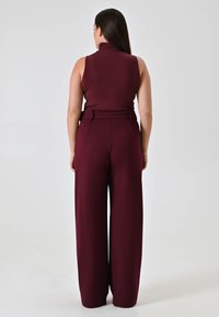 Haut sans manches bordeaux avec un col montant, associé à un pantalon ample. Tissu lisse, taille ceinturée, design minimaliste et sans motifs visibles.