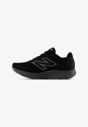Scarpa da corsa nera New Balance con tomaia in mesh, grande logo "N", suola intermédia con motivo e dettagli verdi sulla suola e sull'etichetta della linguetta.