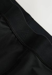 Close-up of a black garment waistband with textured stitching and a subtle triangular logo embroidered on the fabric.