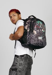 Mochila negra con gráficos de estilo graffiti, que incluyen un ciclista de BMX. Tiene un acento de camuflaje y tirantes acolchados para mayor comodidad.