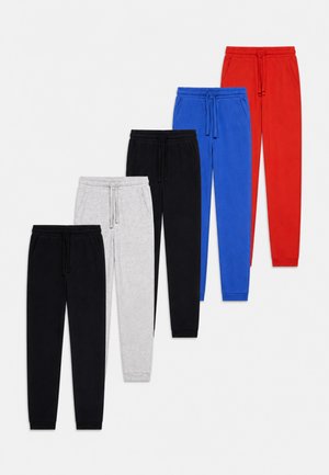 Cinq paires de pantalons de survêtement en noir, gris clair, noir, bleu et rouge, disposées en diagonale sur un fond blanc.