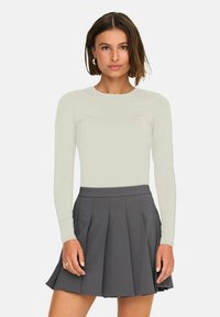 Maglietta a maniche lunghe di un leggero beige abbinata a una gonna plissettata grigia scura. Il materiale sembra liscio, con un design aderente e un colletto rotondo.