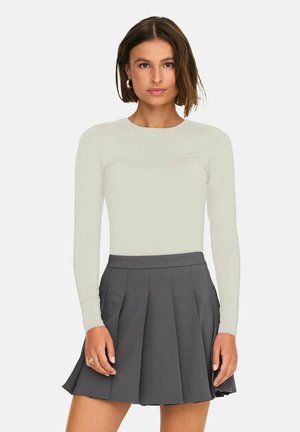 Maglietta a maniche lunghe di un leggero beige abbinata a una gonna plissettata grigia scura. Il materiale sembra liscio, con un design aderente e un colletto rotondo.