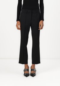 Black tailored trousers with a straight leg, featuring a flat front, belt loops, and a smooth texture, paired with black pointed-toe heels.