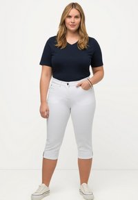 Top corto de cuello en V color navy con mangas cortas, combinado con pantalones capri blancos con aberturas laterales, y calzado deportivo blanco. Textura de tela suave.