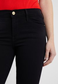Black denim jeans with a fitted design, featuring a gold button closure, subtle stitching, and front pockets.