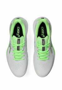 Baskets de sport blanches avec des lacets et des accents vert vif, présentant un dessus texturé avec des perforations pour la respirabilité et un col rembourré.