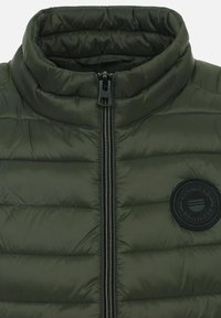 Grüne gepolsterte Jacke mit hohem Kragen, Frontreißverschluss und einem runden schwarzen Logopatch auf der linken Seite. Gesteppte Struktur im gesamten Kleidungsstück.