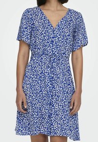 Niebieska sukienka w kwiaty z dekoltem w kształcie litery V, krótkimi rękawami i wiązanym w pasie. Tkanina jest lekka z białymi wzorami kwiatów i liści.