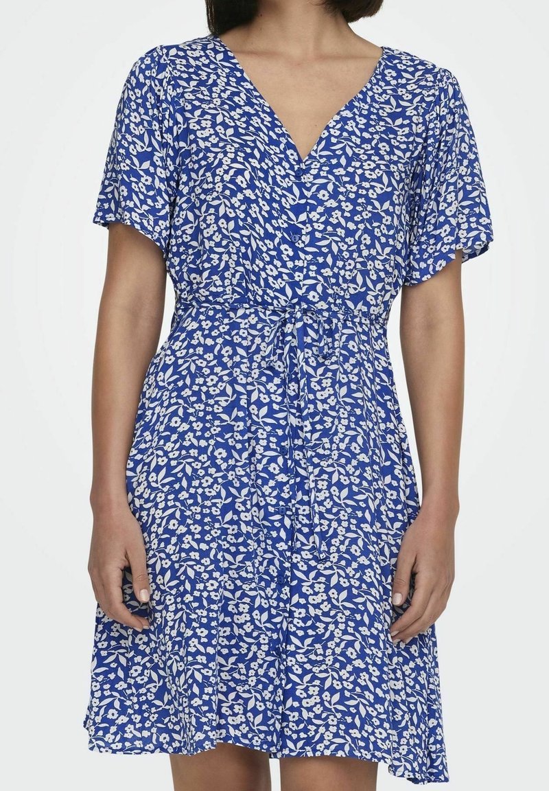 Niebieska sukienka w kwiaty z dekoltem w kształcie litery V, krótkimi rękawami i wiązanym w pasie. Tkanina jest lekka z białymi wzorami kwiatów i liści.