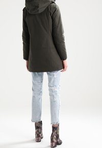 Parka verte à capuche au design léger, associée à un jean bleu clair déchiré et des bottines à talons à motif floral.