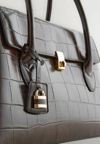 Brown crocodile-embossed leather handbag with smooth texture, featuring gold hardware, a flap closure, and a decorative lock detail.