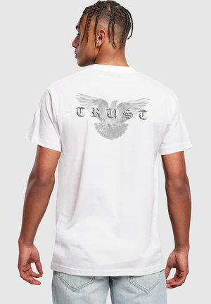 Weißes Baumwoll-T-Shirt mit kurzen Ärmeln. Auf dem Rücken befindet sich eine graue Grafik einer Taube mit ausgebreiteten Flügeln und dem Wort "VERTRAUEN" in fetter Schrift darunter.