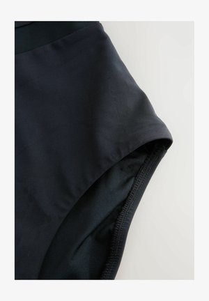 Tuvplāns melnā auduma peldbiksītēm ar redzamu šuvi un jostu uz gaiša fona.