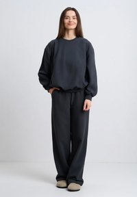 Ciemnoszara, oversize bluza z prążkowanymi ściągaczami, zestawiona z pasującymi szerokimi spodniami. Miękki materiał o luźnym kroju i minimalistyczne detale.