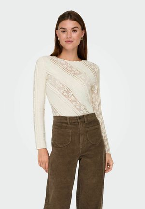 Off-white spetsblus med långa ärmar, med ett randigt mönster. Kombinerad med högmidjade, bruna kordflosbyxor med fickor.