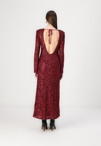 Long burgundy sequin dress with a low back, long sleeves, and a ribbon tie detail at the neck. Smooth texture with a fitted silhouette.