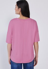Camicia rosa a maniche corte con un fit rilassato, caratterizzata da un colletto rotondo e una texture liscia, abbinata a jeans in denim blu.