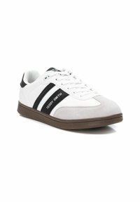 Zapatilla blanca con acentos en negro y gris, materiales de ante y cuero texturizados, suela plana de goma marrón y cierre de cordones. Logo "Teddy Smith" destacado.