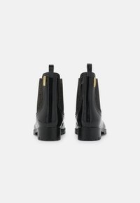 Zwarte Chelsea boots van glanzend lakleer met getextureerde elastische zijkanten, voorzien van aantrekhulpjes en een chunky zool voor extra grip.