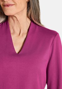 V-hals lange mouw top in levendige magenta stof met een gladde textuur en een strakke pasvorm, die een schone silhouet zonder patronen toont.