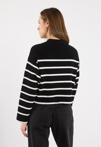 Svart-hvitt stripete kort trøye med ribbet tekstur og rund hals. Kombinert med høy midje svarte jeans, sett fra baksiden.