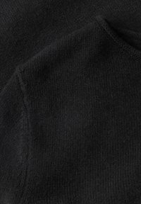 Gros plan sur un tissu noir doux avec une texture visible et des coutures le long d'une couture et du bord du col.