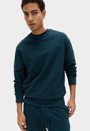Dark teal sweatshirt in soft fabric, featuring a round neckline, ribbed cuffs, and a relaxed fit, paired with matching pants.