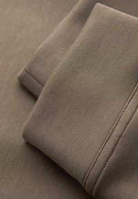 Zbliżenie złożonego brązowego materiału z widocznymi szwami i gładką teksturą.