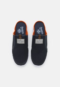Scarpe slip-on in rete blu navy con dettagli arancioni, caratterizzate da un motivo testurizzato e un'etichetta logo argentata sul lato. Suola bianca.