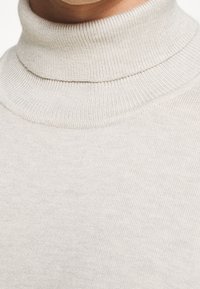 Ljusbeige polokragetröja gjord av ribbad stickad tyg, med hög krage och mjuk textur. Enkelt och minimalistiskt design.