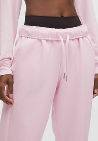 Rózsaszín melegítőnadrág, rugalmas derékkal és húzózsinórral, puha tapintással és oldalsó zsebekkel. Hozzá csatlakozó hosszú ujjú felső látható.