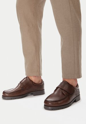 Brązowe skórzane buty z paskiem na podbiciu, charakteryzujące się gładkim wykończeniem, przeszyciami i grubą gumową podeszwą.