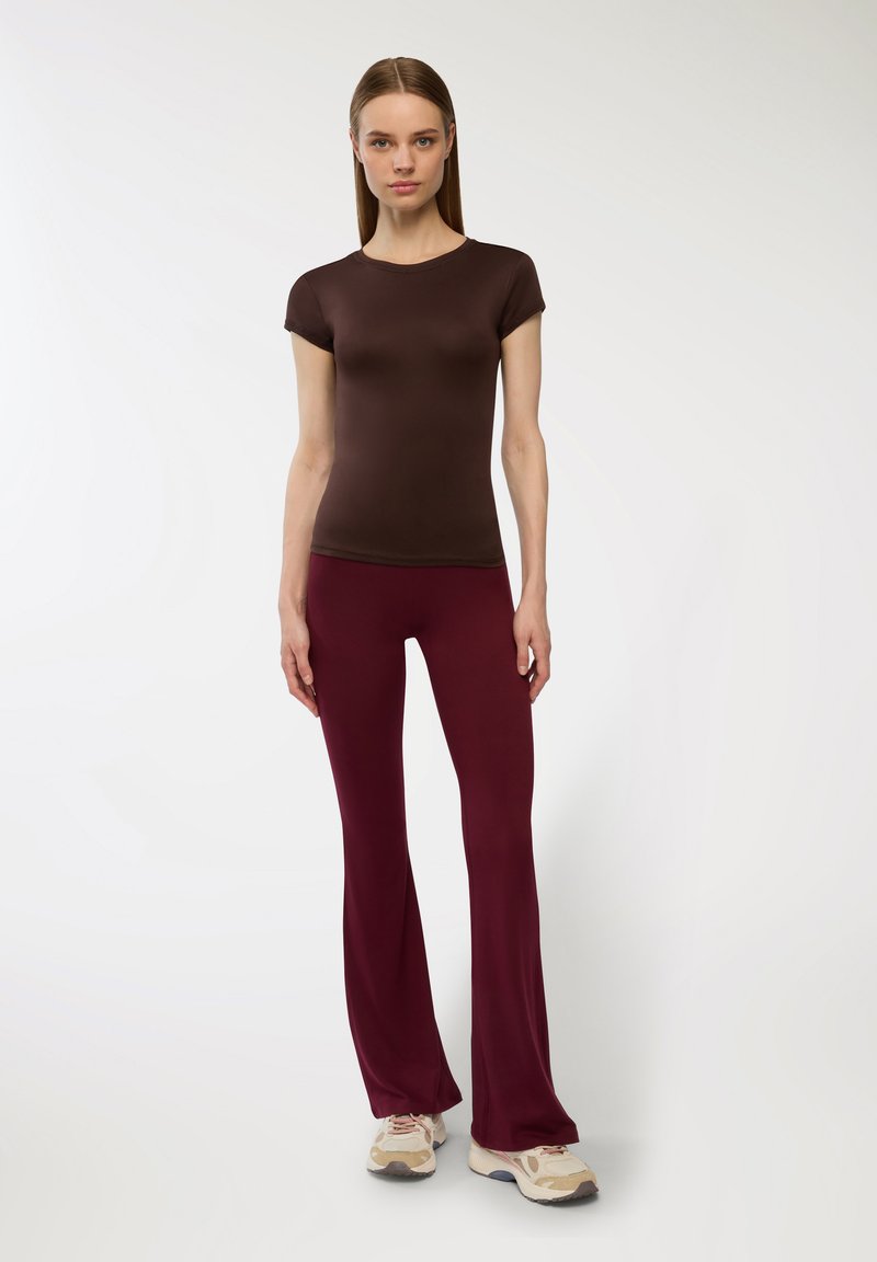 Brązowy krótki top dopasowany z krótkim rękawem zestawiony z burgundowymi spodniami w kant i neutralnymi trampkami, na jednolitym tle.